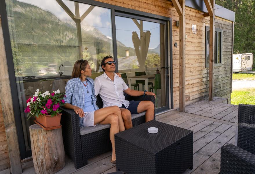 Coppia rilassata su veranda di legno, circondata da montagne e fiori colorati.