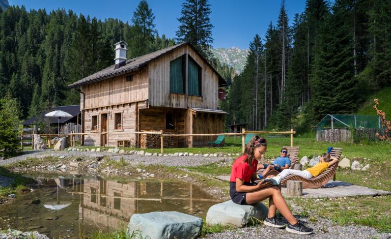 Ragazzi rilassati in montagna, vicino a uno chalet di legno e un laghetto.