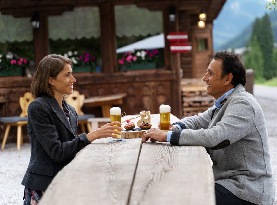 Two people toast with beer in a mountain setting.