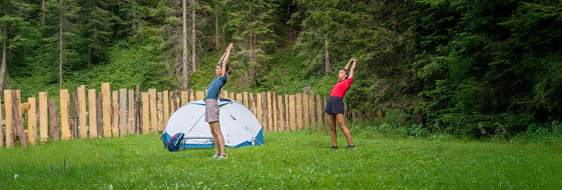 Due persone fanno stretching vicino a una tenda nel bosco.